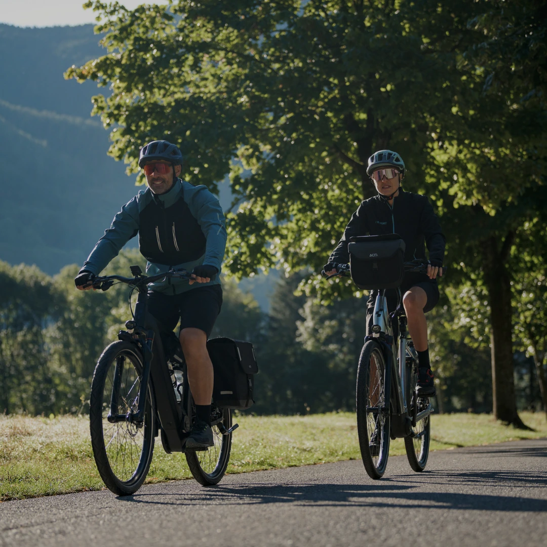 Zwei Radfahrer fahren entspannt auf einem sonnigen Landweg mit Ausblick auf die Berge
