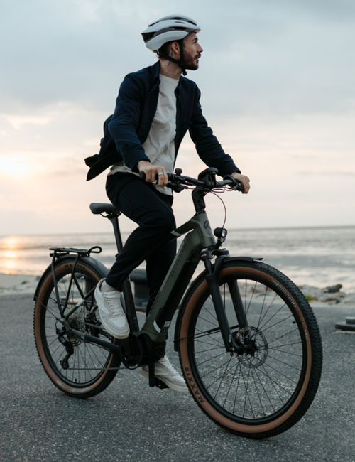 Mann fährt entspannt auf einem E-Bike bei Sonnenuntergang entlang der Küste.